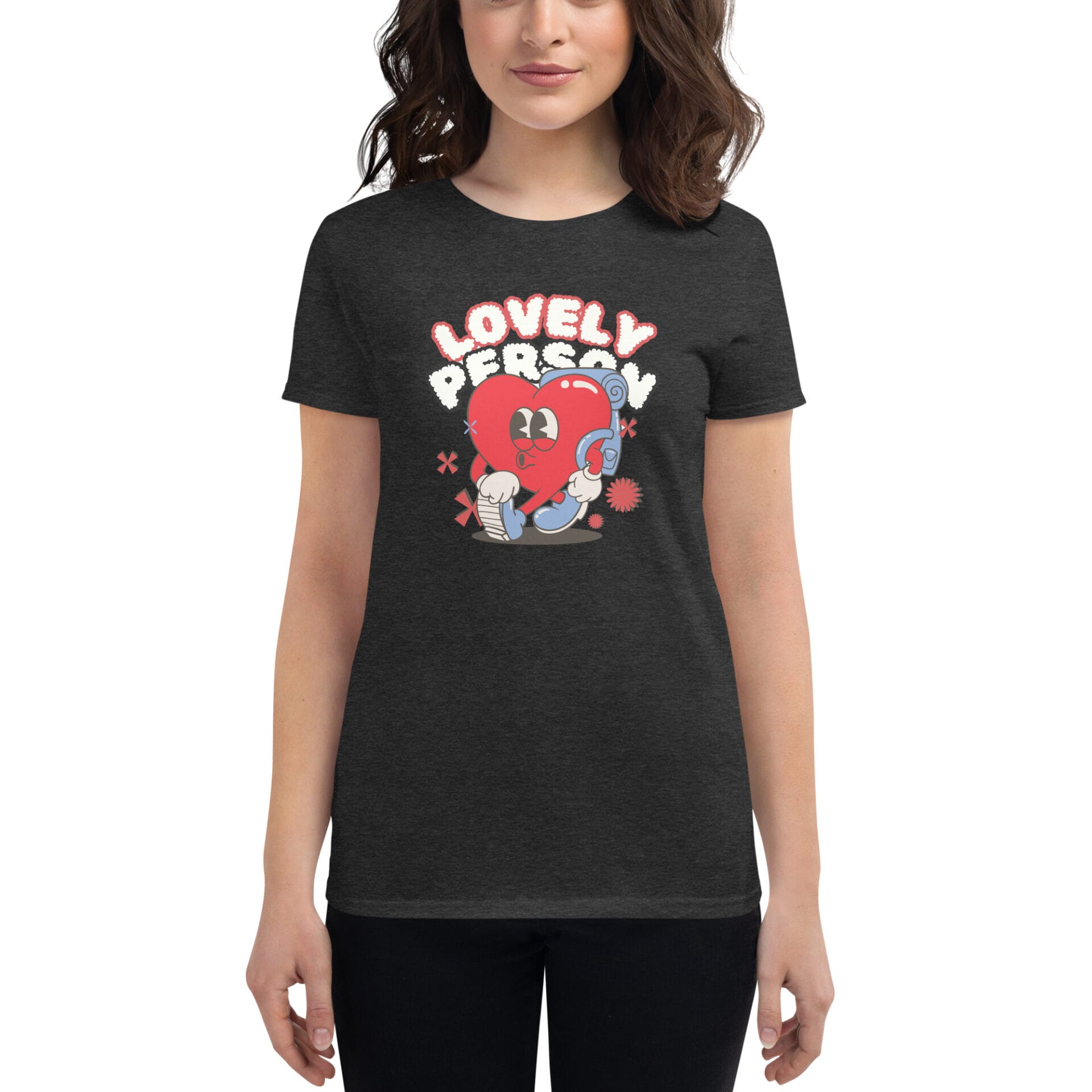 A person wears a dark t-shirt featuring a colorful graphic of a happy heart character with the text "LOVELY PERSON" above it in a playful font set against a neutral background.