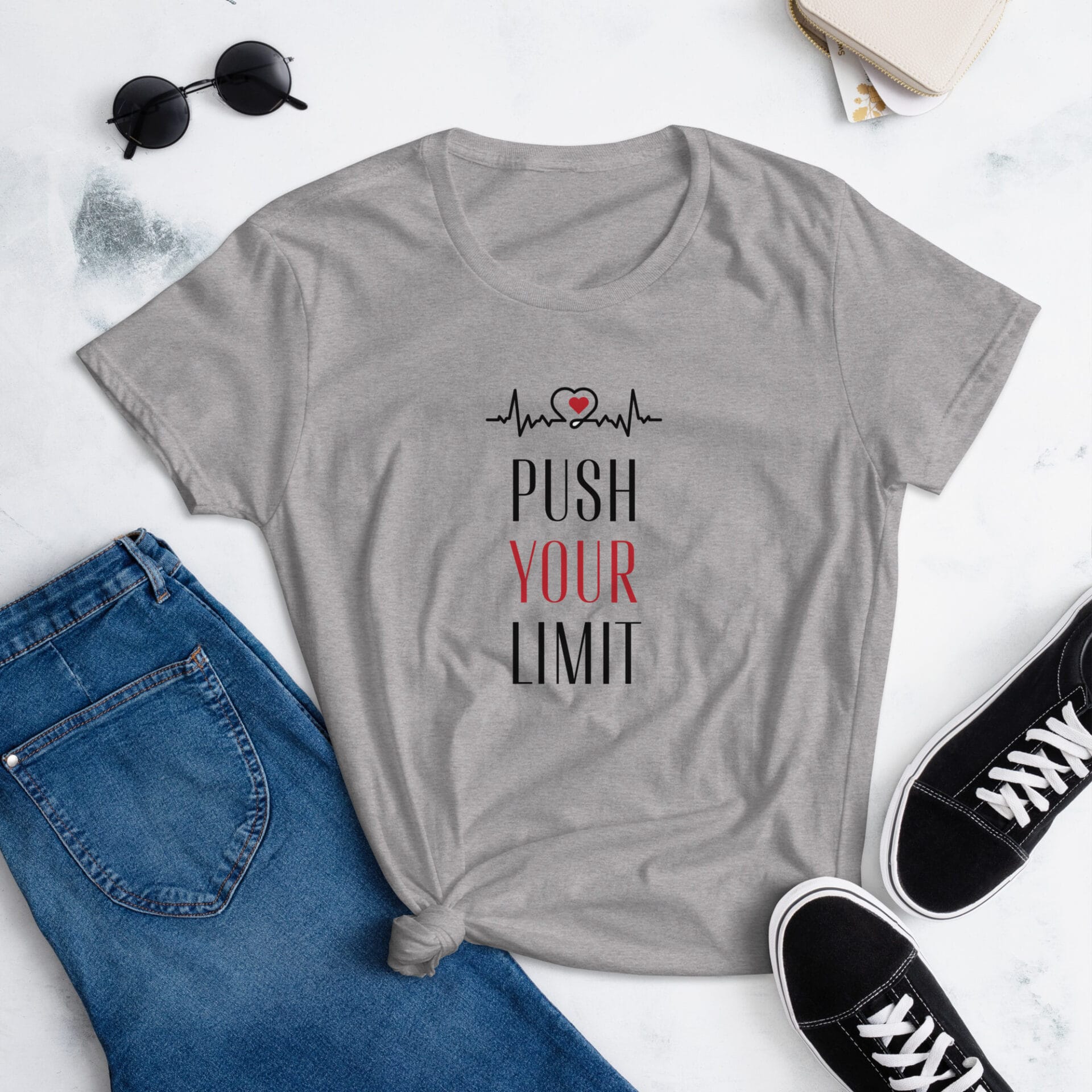 A gray t-shirt lays on a flat surface alongside blue jeans and black sneakers The shirt features the text PUSH YOUR LIMIT with a heartbeat line and a heart graphic