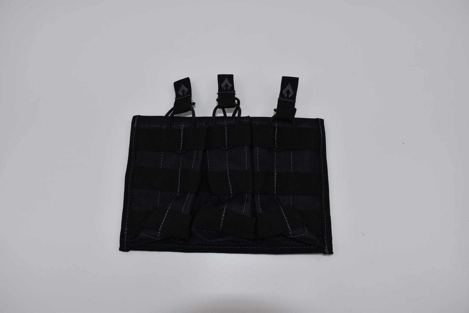 A black tactical pouch with expandable sections and three attachment points sits flat on a white surface  designed for organizing and securing equipment or accessories in various outdoor or tactical contexts.