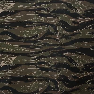 A camouflaged fabric with a wavy pattern featuring various shades of green black and brown is spread out flat highlighting a military style design often used for clothing or gear.